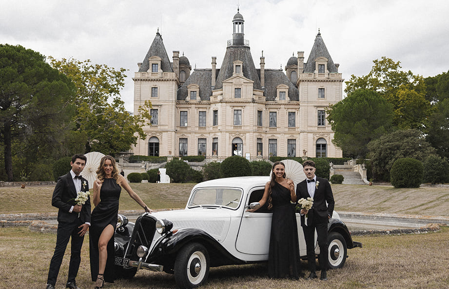 Invités élégants posant devant une voiture de collection lors d’un mariage au château.