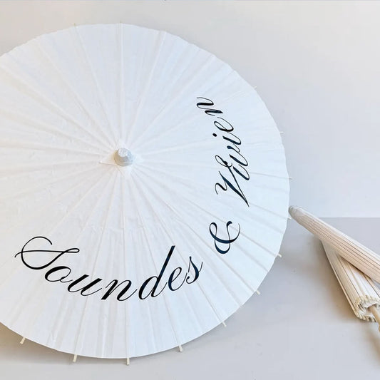 Ombrelle de mariage personnalisée en papier blanc et manche en bois avec prénoms des mariés, accessoire photo élégant et romantique.